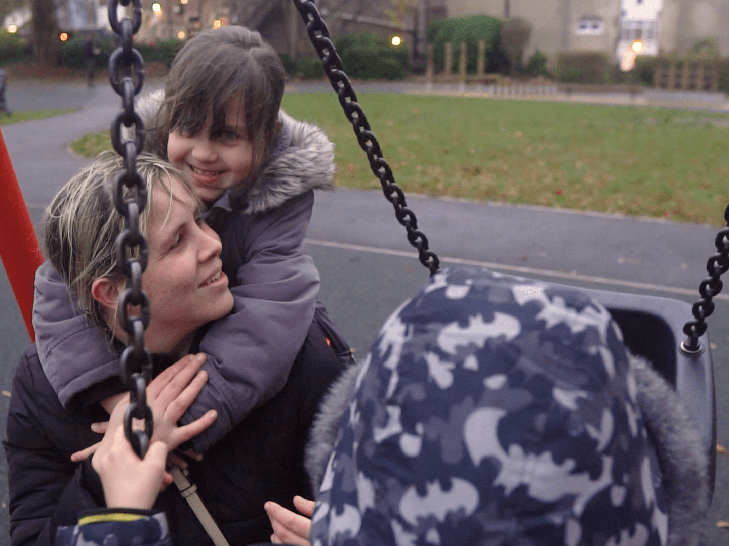 little girl hugging her mum on a swing in a playground in winter