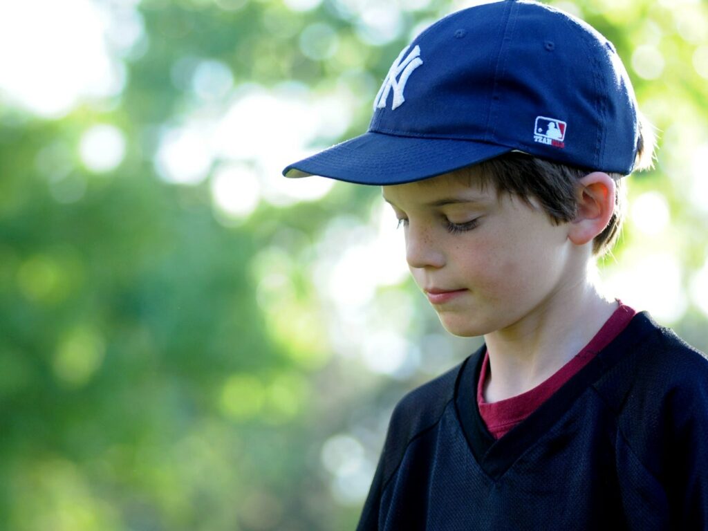 sad boy standing outside wearing Yankees baseball cap