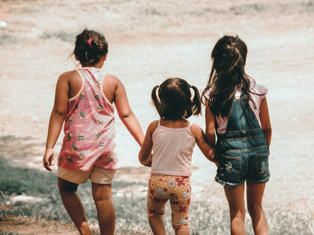 three young children walking in a park holding hands