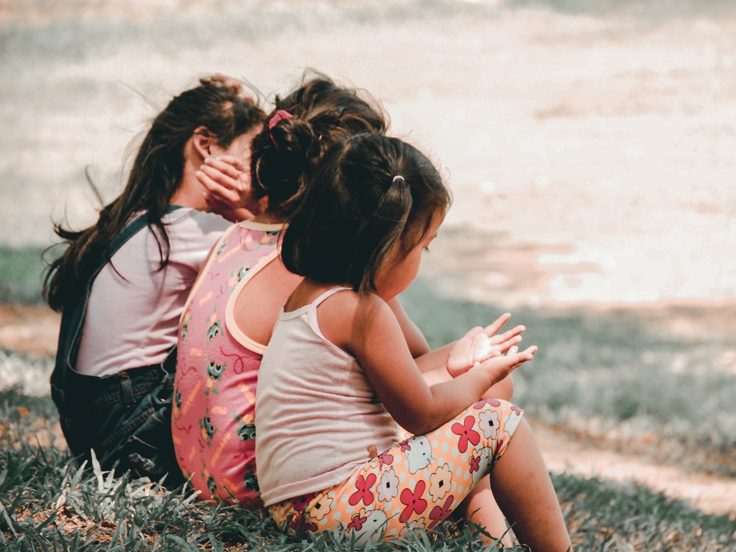 three little girls sitting in a park 