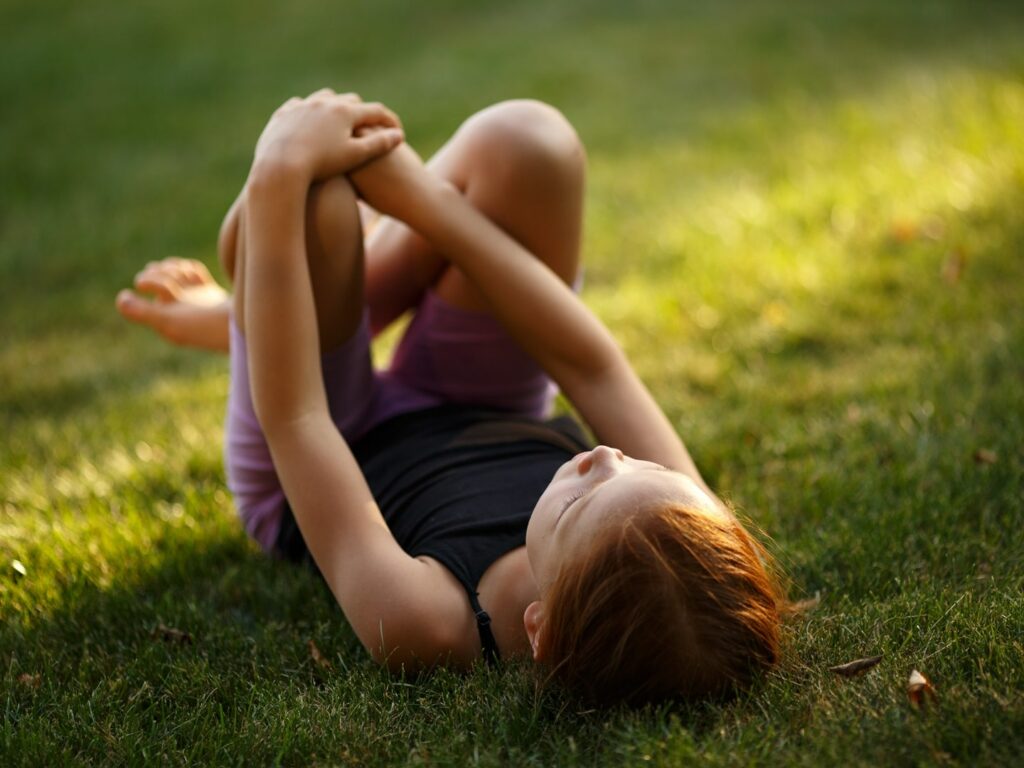 young girl with red hair lying on green grass