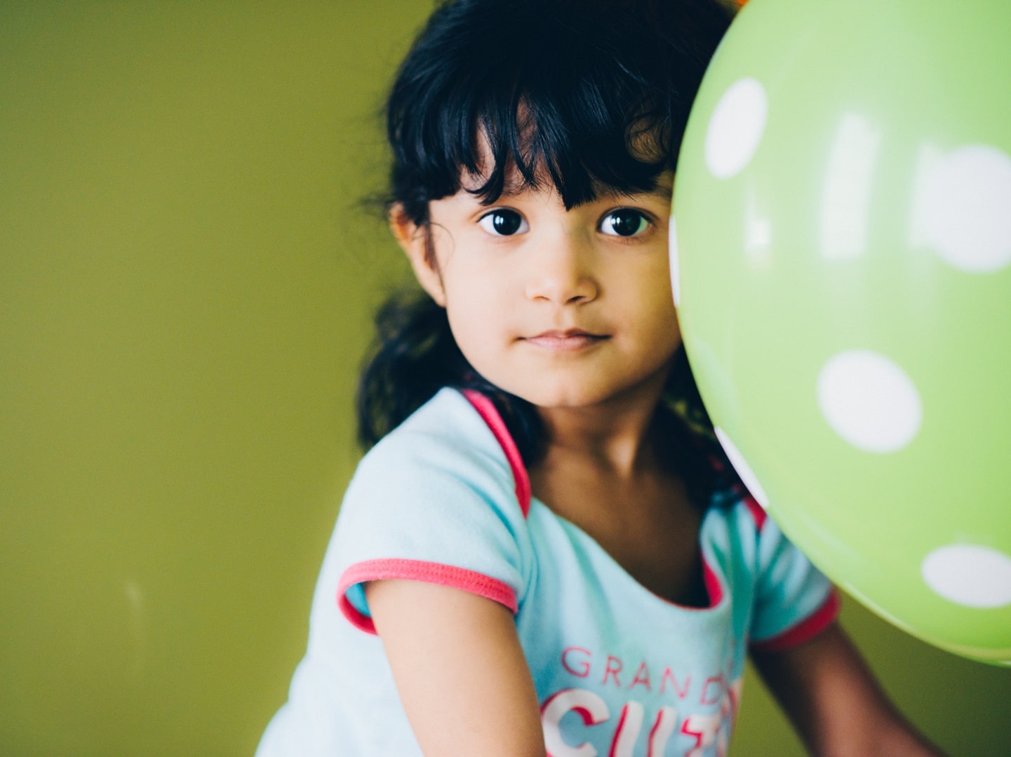 little girl with dark hair and brown eyes standing next to a green balloon