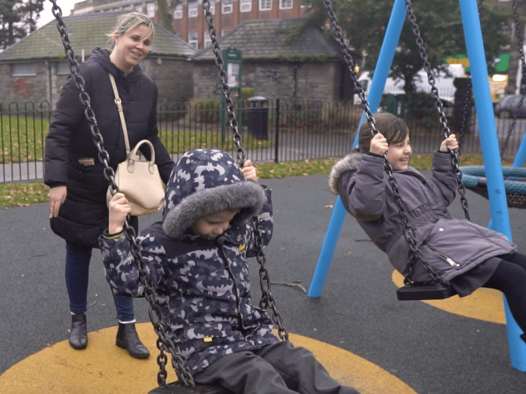 mum pushing children on swings in playground in winter