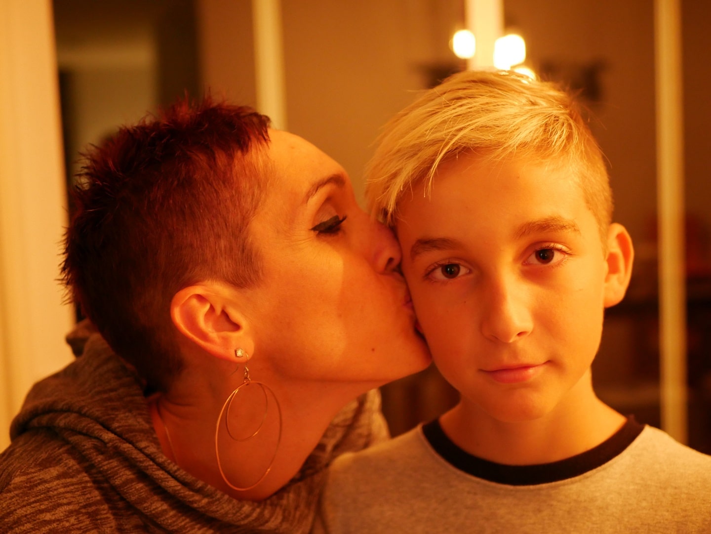 mum with hoop earrings kissing teenage son on the cheek