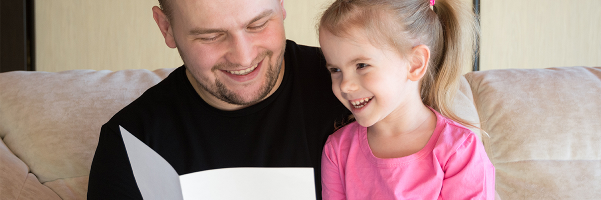 smiling dad with beard reading story to little girl in pink top