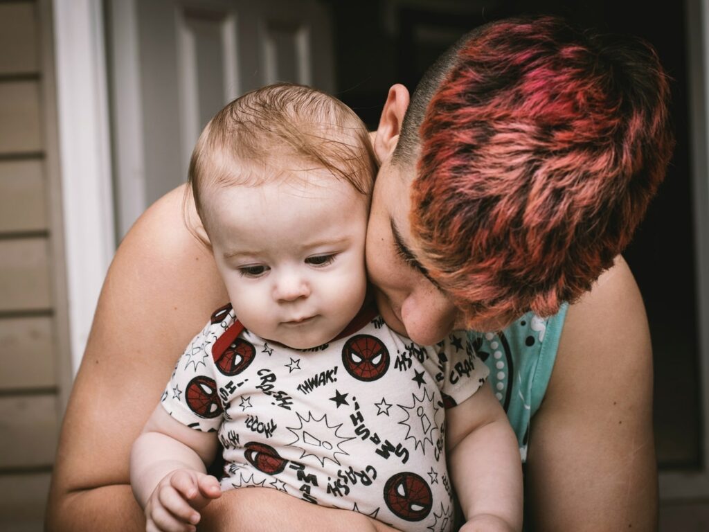 man with red hair holding baby son with spiderman onesie
