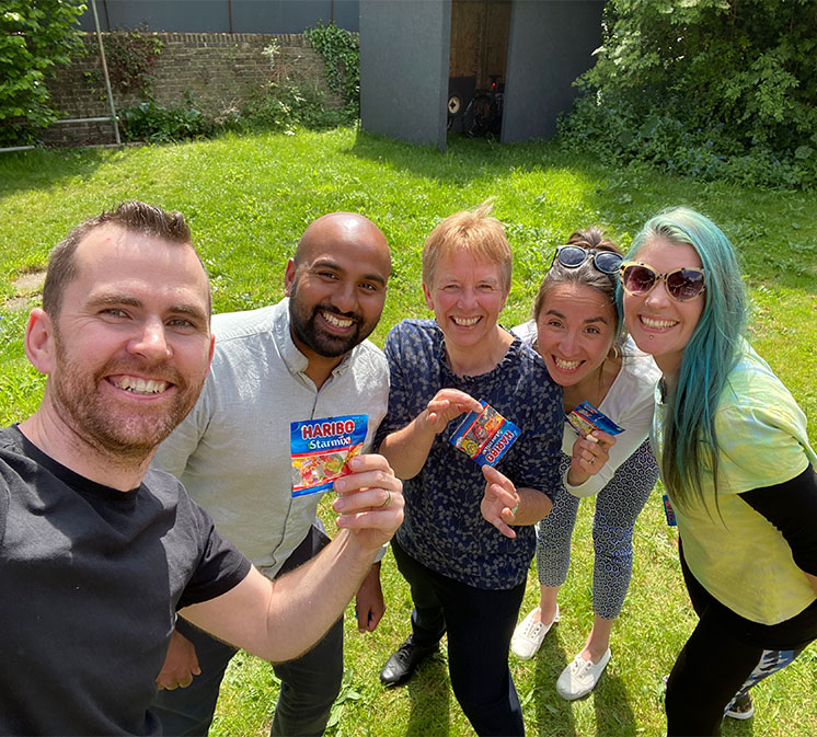 smiling friends in garden holding Haribo sweets at Kids Matter charity team day